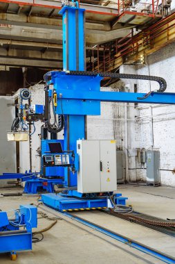 Industrial automation equipment in a factory during daytime work. A blue robotic arm and control panel are set up in a factory for automated tasks and assembly processes. clipart