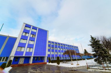 Kış manzarasında karla çevrili modern mavi bina. Canlı mavi bir yapı, bulutlu gökyüzü ile bir kış günü sergilenen karın ortasında dimdik duruyor..