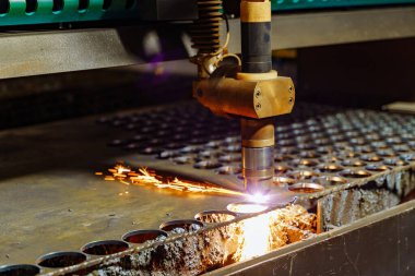 Geceleri bir üretim tesisinde metal parçaları kesen lazer. Lazer kesici, metal bileşenleri şekillendirir ve yoğun bir fabrika ortamında gece saatlerinde kıvılcımlar üretir..