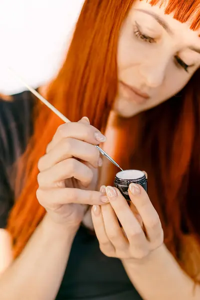 stock image Woman applying makeup with an application tool in natural light. A woman focuses on applying makeup carefully