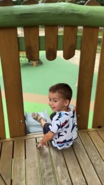 Çocuk parkında kayan bir çocuğun arka görüntüsü. Çocuk aşağı kayıyor ve kameraya doğru dönüyor. Dikey video.