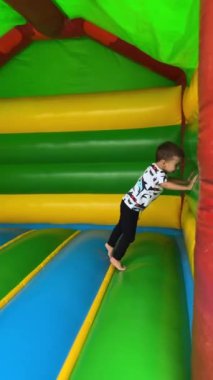 Enerjik erkek bebek şişme oyun evinde neşeyle koşar, düşer ve yuvarlanır. Aktif eğlenceli zaman harcamaların kutlu olsun. Dikey video.
