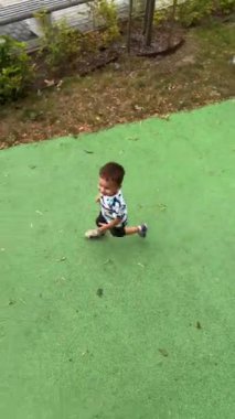 Oyun parkında zıplayan sevimli beyaz bir çocuk. Açık havada oynayan çocuğun en iyi görüntüsü. Dikey video.