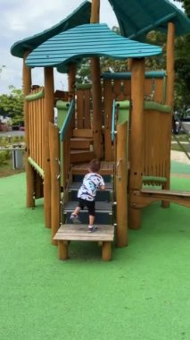 Küçük çocuk dördünde de tahta merdivenlerden çıkıyor. Bebek yazın çocuk parkında oynuyor. Dikey video.
