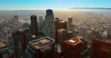 Modern Los Angeles 'ın finans merkezi tepeden. Helikopter platformlarıyla gökdelenlerin üzerinden ABD Bank Tower binasına yaklaşıyoruz. Metropolün alçak katlı manzarası arka planda sisle kaplıdır..