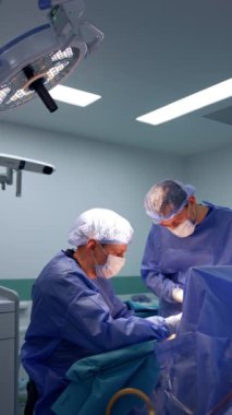 Hastaya bakan konsantre erkek cerrah. İki doktor birbirleriyle iş birliği yaparak ameliyat yapıyorlar. Dikey video.