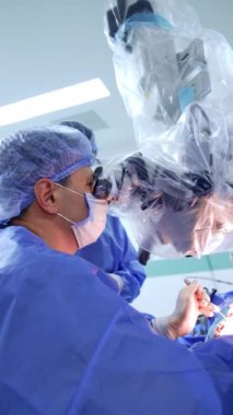 Kafkas erkek doktor hastayı ameliyat ederken mikroskoba dikkatlice bakıyor. Doktor modern cerrahi aletler tutuyor. Dikey video.