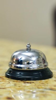 Otel zili resepsiyon masasında. Adamın eli oteldeki resepsiyonisti aramak için zil tuşuna basıyor. Müşteri metal alarma dokunuyor. Yakın plan. Dikey video