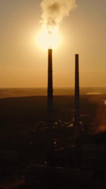 Fabrika atmosferi zararlı emisyonlarla kirletir. Doğa arasındaki sanayi bitkisinin silueti. Duman gün batımında borulardan çıkar. Dikey video