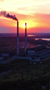 Akşam doğasında sanayi bölgesi. Gün batımında fabrika bacasından siyah duman dökülüyor. Nehir kenarındaki fabrika, yoğun bulutların arka planına karşı. Çevre kirliliği. Dikey video
