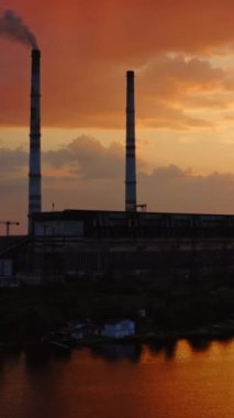 Turuncu arka plandaki fabrika. Gün batımında nehrin üzerinde zararlı bir kimyasal tesis. Kırsal bölgedeki büyük sanayi bölgesi. Dikey video