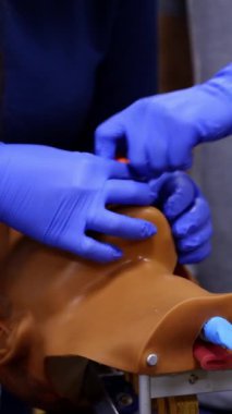 Kuklanın kafasında eğitim becerileri. Tıp eğitmeni, bir öğrencinin kafasına tıbbi prosedür uygular. Pratisyen bir bebekle öğreniyor. Yakın plan. Dikey video