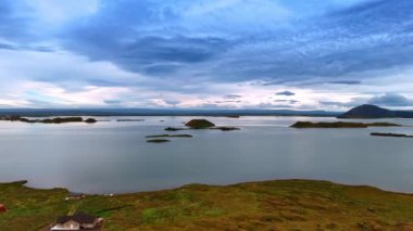 Üzerinde bazı kulübeler olan kayalık sahilde yükseliyor. Sudan çıkan taşlarla sakin su manzarasını gözler önüne seriyor. İzlanda doğası.