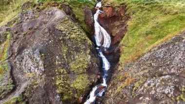 Kayaların arasından akan küçük bir şelale. Dağların üzerinden yosunla kaplı bir dron yükseliyor. Bir taş parçası sudan fırlıyor..