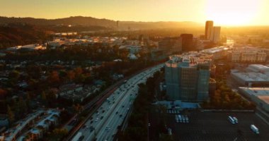 Yoğun çok şeritli otobanın üzerinde uçarken birden fazla araba geçiyor. Güneşin batışı Los Angeles, California, ABD manzarasının üzerinde..