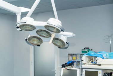 Parlak cerrahi ışıkları olan modern ameliyathane. Ameliyat masasının üzerinde parlak cerrahi ışıklar asılı. Karmaşık tıbbi işlemler için donanımlı temiz ve steril bir ortam sergiliyorlar..