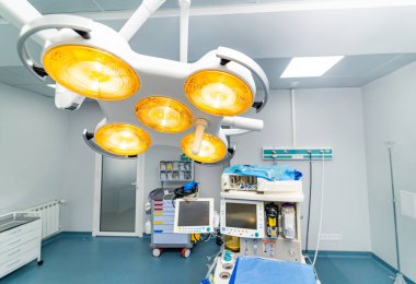 Modern ışıklar ameliyathaneyi aydınlatır. Steril bir ameliyathanede, ameliyat için hazır tıbbi aletler ve monitörlerle parlayan parlak ışıklar..