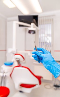 Modern klinikte aletleri olan bir dişçi. Mavi eldivenli bir diş hekimi, kırmızı ve beyaz ekipmanlı modern bir klinikte çalışmaya hazırlanıyor..
