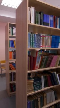 Kütüphanedeki ahşap kitaplıklar. Kütüphane odasındaki kitaplıklarda farklı kitaplar var. Eğitim ve bilgi kavramı. Dikey video