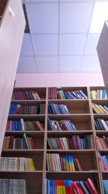 Kütüphane kitapları raflara istiflenmiş. Kütüphanede kitapları olan sıra sıra kitaplıklar. Eğitim, okul veya üniversite öğrenme konsepti. Kamera geri gidiyor. Dikey video