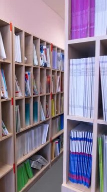 Modern kitapçı. Eğitim edebiyatı kütüphanedeki öğrenciler için raflarda duruyor. Kapalı alanda bir sürü kitabı olan ahşap kitaplıklar. Dikey video