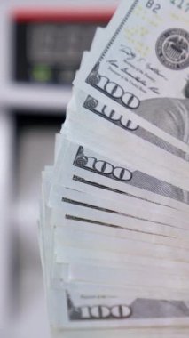 Kadının elinde Amerikan parası var. Otomatik sayaç makinesinin bulanık arka planında 100 dolarlık banknotlar var. Finans konsepti. Yakın plan. Dikey video