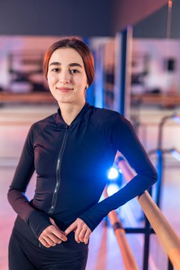 Modern bir stüdyoda zarif bir şekilde poz veren genç dansçı. Genç bir dansçı, parlak, çağdaş bir stüdyoda, bale barının yanında güvenle duruyor.