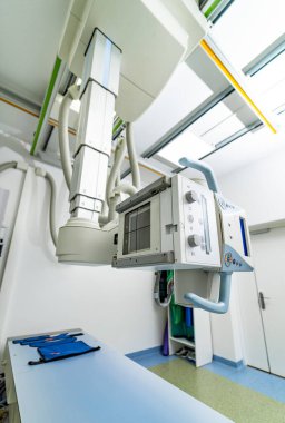 Parlak bir tıbbi tesiste modern bir röntgen cihazı. Üst düzey bir röntgen cihazı iyi aydınlatılmış bir tıp odasında tavandan sarkıyor. Tanısal görüntüleme işlemleri için hazır..
