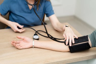 Hemşire muayenede tansiyonunu ölçer. Bir sağlık uzmanı, klinik ortamda hastanın kan basıncını ölçer ve düzenli olarak sağlık kontrollerini sağlar..