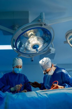 Modern bir hastane ameliyatında cerrahlar. İki yetenekli cerrah, ameliyathanede karmaşık bir cerrahi müdahale sırasında bir hastaya dikkatle odaklanır..