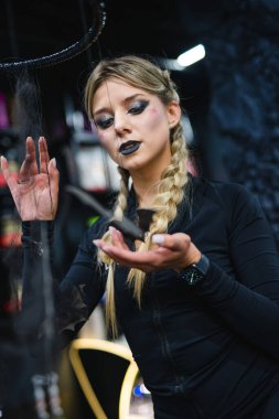 Koyu renk elbiseli kadın örümcek ağlarıyla sanat yaratıyor. Örgülü saçlı ve koyu renk makyajlı bir kadın sanatsal bir düzenleme yapıyor. Zarif örümcek ağları kullanarak yaratıcılığını gösteriyor..