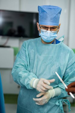 Cerrah steril ameliyata hazır. Tam koruyucu donanımlı bir cerrah temiz bir hastane ortamında hassas cerrahi aletler hazırlar..