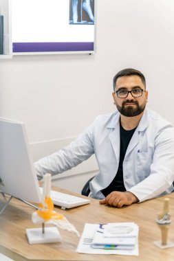 Modern bir klinikte hastaya danışmanlık yapan bir doktor. Bir sağlık uzmanı masasında oturuyor, tıbbi görüntülemeyi incelerken teşhisi tartışmaya hazır.