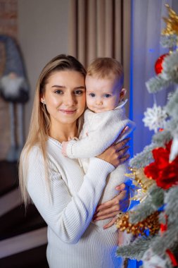 Anne ve bebek Noel ağacının yanında. Bir anne bebeğini güzel dekore edilmiş bir Noel ağacının yanında tutarken gülümser.