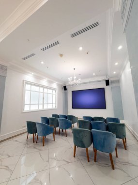 Mavi sandalyeli ve ekranlı modern konferans odası. Parlak bir konferans odasında büyük bir ekranın etrafına dizilmiş mavi sandalyeler yer alır.