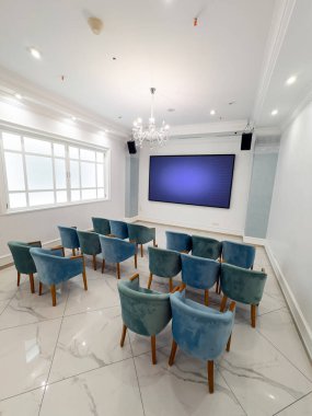 Mavi sandalyeli ve ekranlı modern konferans odası. Gündüzleri sunumlar veya toplantılar için ideal büyük ekrana bakan sıra sıra mavi sandalyelerin yer aldığı şık bir konferans odası.