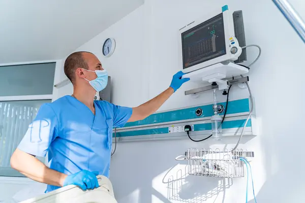 stock image Pro monitors patient's vitals in hospital. A healthcare worker checks vital signs on a monitor while providing care in a hospital room during the morning shift.