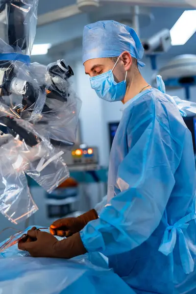 stock image Surgeon operates in sterile conditions. A surgeon in a blue surgical gown and mask focuses on a procedure, ensuring precision in a sterile operating room setting.