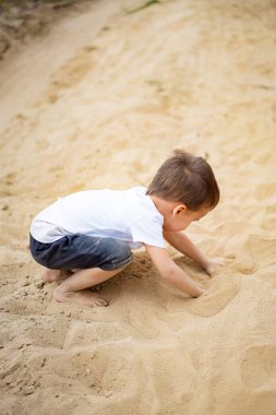 Güneşli bir günde kumsalda oynayan küçük bir çocuk. Bir çocuk sıcak kumu kazmaktan zevk alır.
