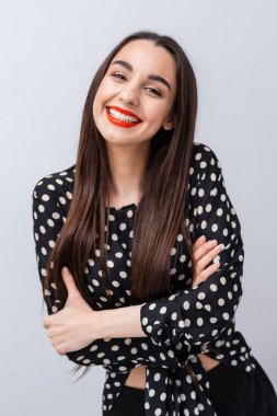 İçerideki puantiyeli bluzla güvenle gülümseyen genç bir kadın. Uzun saçlı genç bir kadın ışıl ışıl gülümsüyor, puantiyeli gömlek giyiyor..