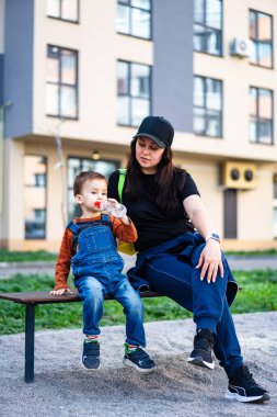 Anne ve oğlu güneşli bir bankta dondurma yiyorlar. Bir kadın ve küçük oğlu, güneşli bir açık hava parkında dondurmanın tadını çıkarırken bir bankta oturup tatlı bir anı paylaşıyorlar..