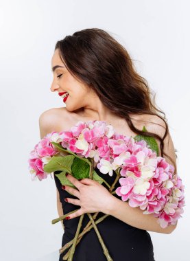 Genç kadın mutlu bir şekilde canlı pembe çiçekleri içeride tutuyor. Uzun saçlı genç bir kadın neşeyle bir buket pembe çiçeği kucaklıyor.