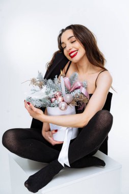 Neşeli kadın modern ortamda şenlikli bir dekora sahip. Beyaz bir platformda zarif bir şekilde oturan bir kadın süslü bir tatil düzenini neşeyle kucaklıyor.