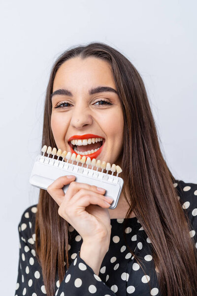 Woman smiles with dental shade guide indoors. A joyful woman with long hair holds a dental shade guide close to her face