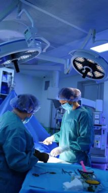 Modern ameliyathanede iki kadın doktor çalışıyor. Cerrah, kesiği dikmek için iğne ve iplikle bir alet tutuyor. Dikey video.