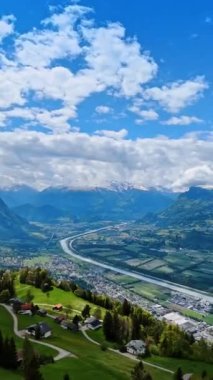 Avrupa, Lihtenştayn 'ın nefes kesici manzarası. Ren Nehri boyunca uzanan şehir manzarası büyüleyici dağlarla çevrilidir. Mavi gökyüzü, panoramanın üstünde birden fazla bulut var. Dikey video.