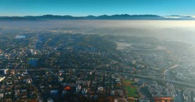 Modern şehri kaplayan hafif sis bulutları arasında uçmak. Gündüz vakti FPV insansız hava aracından Los Angeles şehir manzarasına bak.