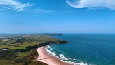 Mavi su manzarası ve gökyüzü ile İrlanda 'nın kayalık kıyılarının çarpıcı manzarası. Tarlaları ve ender evleri olan manzaraya hava perspektifi.