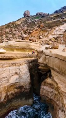 İnsanlar yüksek bir uçurumun kenarında dururlar. İnsansız hava aracı, deniz manzaralı dağdan uzaklaşıyor. Dikey video.