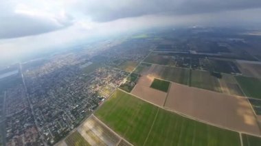 Ortasında dikdörtgen tarlalara bölünmüş tarım arazileri olan geniş bir şehir. Bulutlar arasındaki FPV insansız hava aracı görüntülerinden manzara.